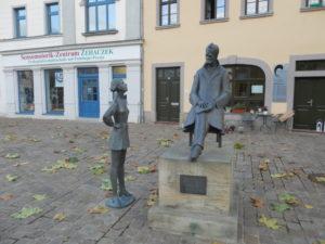Figur von Nietzsche sitzend, links daneben die Figur eines Mädchens