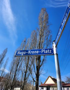 Blaues Straßenschild vor blauem Himmel und Bäumen